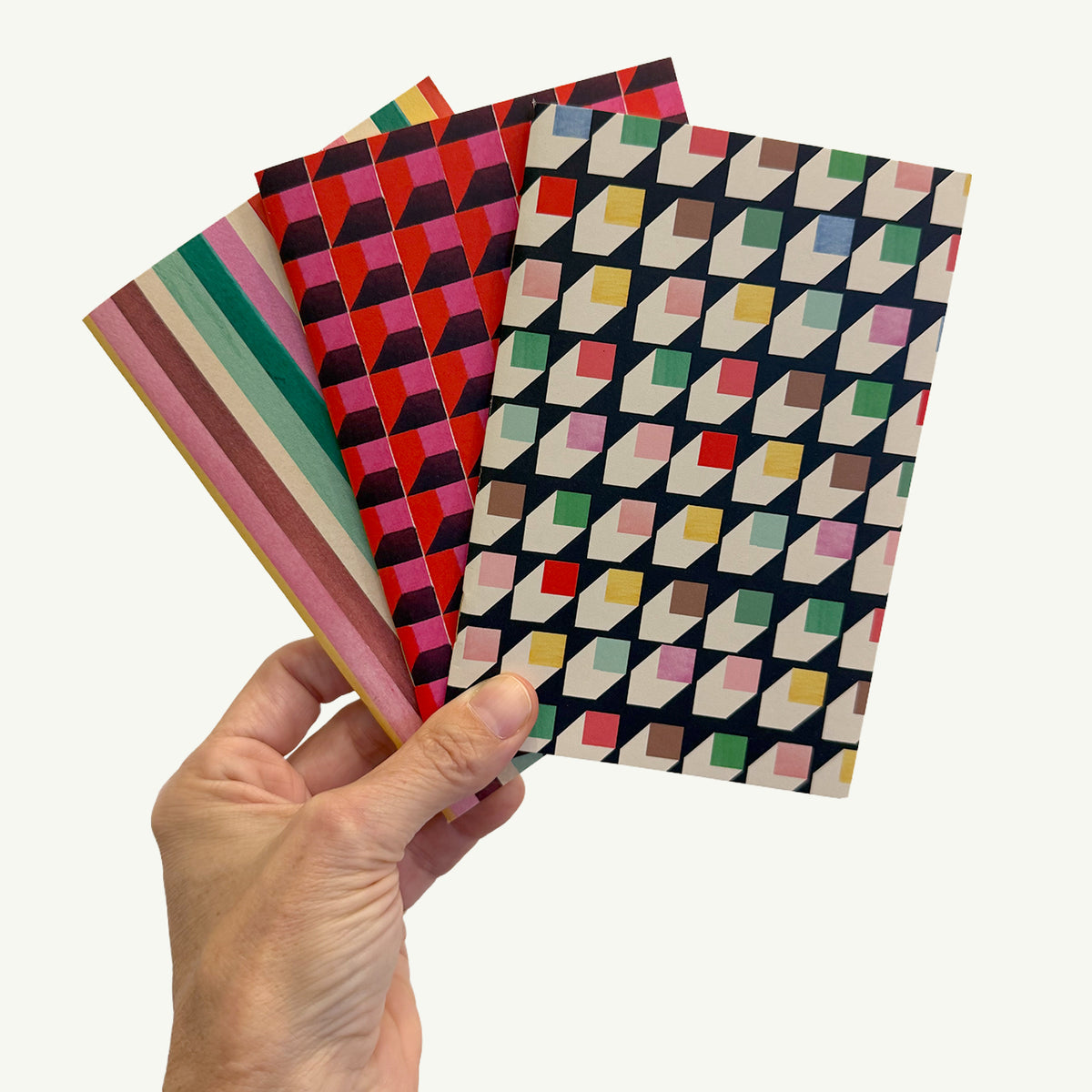 A hand holding a set of 3 Mr. Boddington’s Studio Pocket Notebooks with geometric patterns.