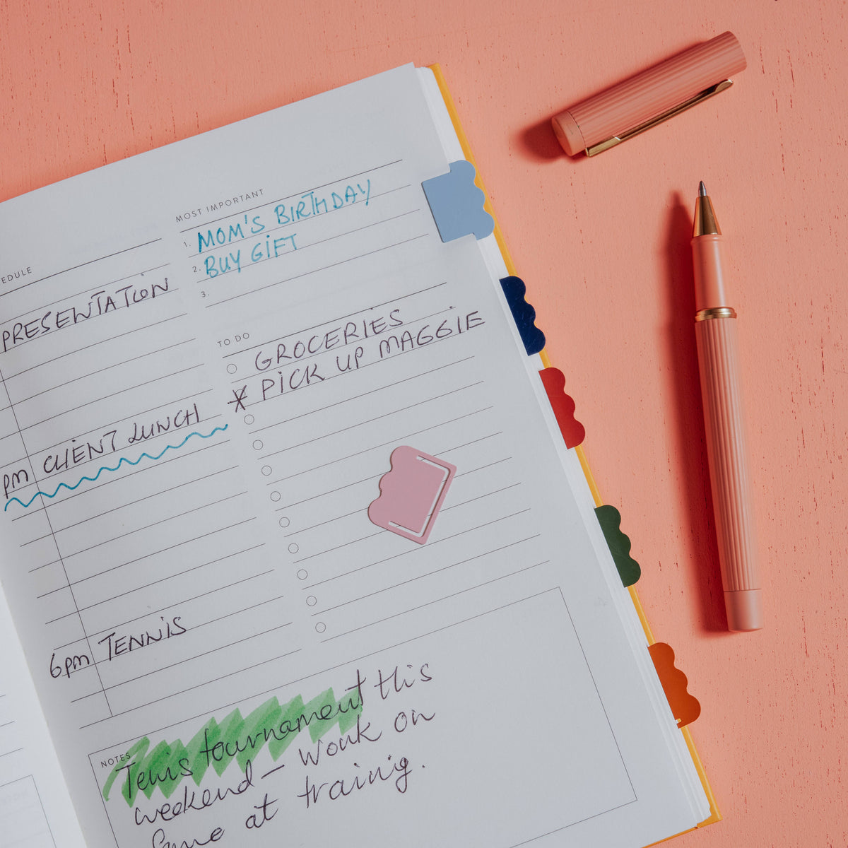 Open planner with notes, pen, Papier Metal Index Tabs (Cloud), on a peach-colored desk.