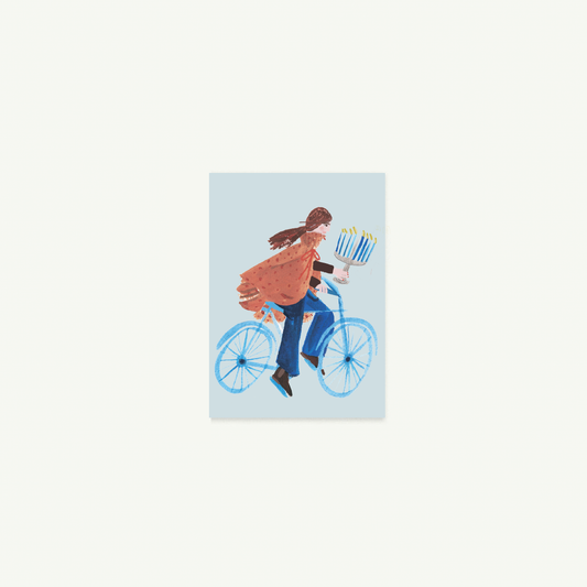 Person rides blue bike with gifts, menorah—Biking You Light Petite Card by Mr. Boddington’s Studio.