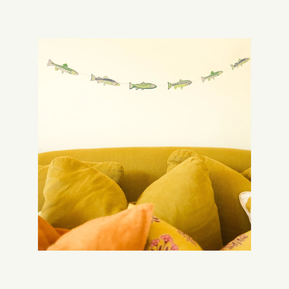 TASTY ANCHOVIES SEWN GARLAND by East End Press hangs above yellow and orange pillows.