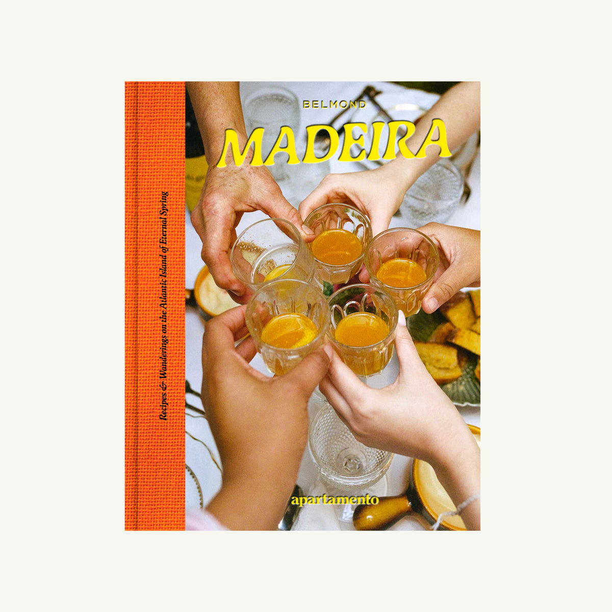 Six hands toast over food beside “Madeira: Recipes & Wanderings” by Apartamento on island cuisine.