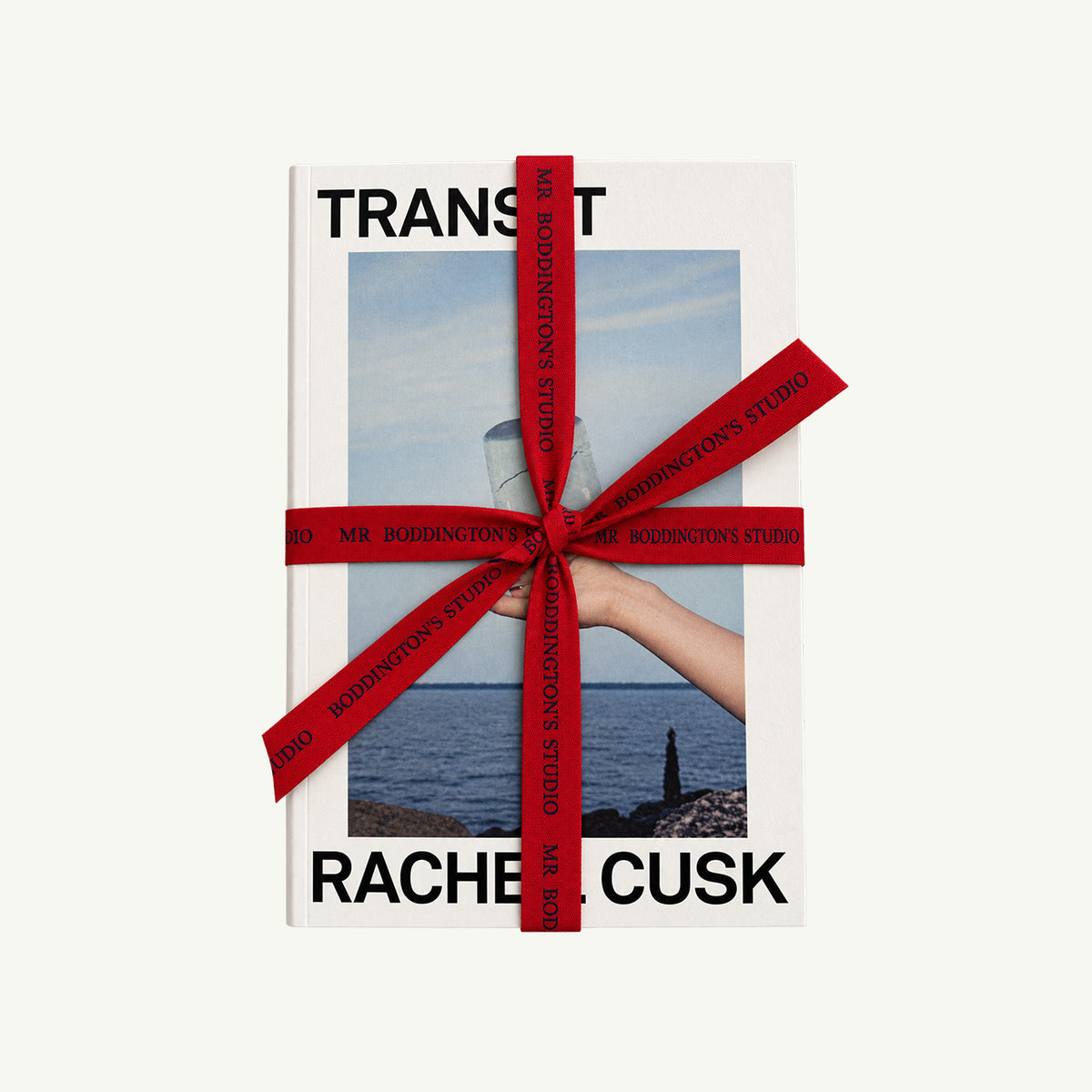 Rachel Cusk Bundle by Macmillan Publishers, tied with red ribbon, hand holds glass before water.